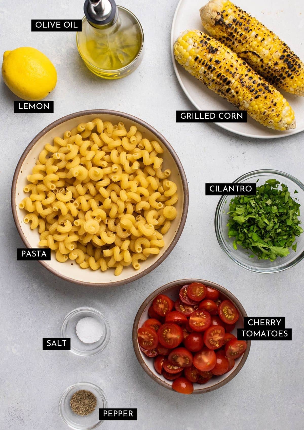 Pasta salad ingredients, organized into individual bowls on a white table.