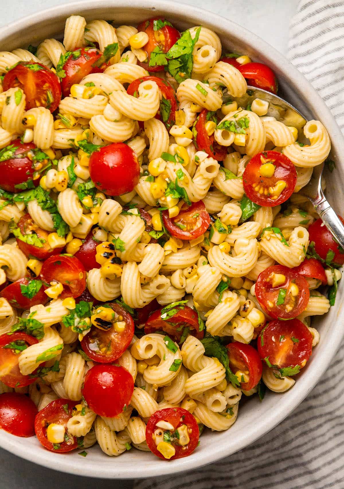 Spoon lifting a scoop of corn and tomato pasta salad out of a bowl.