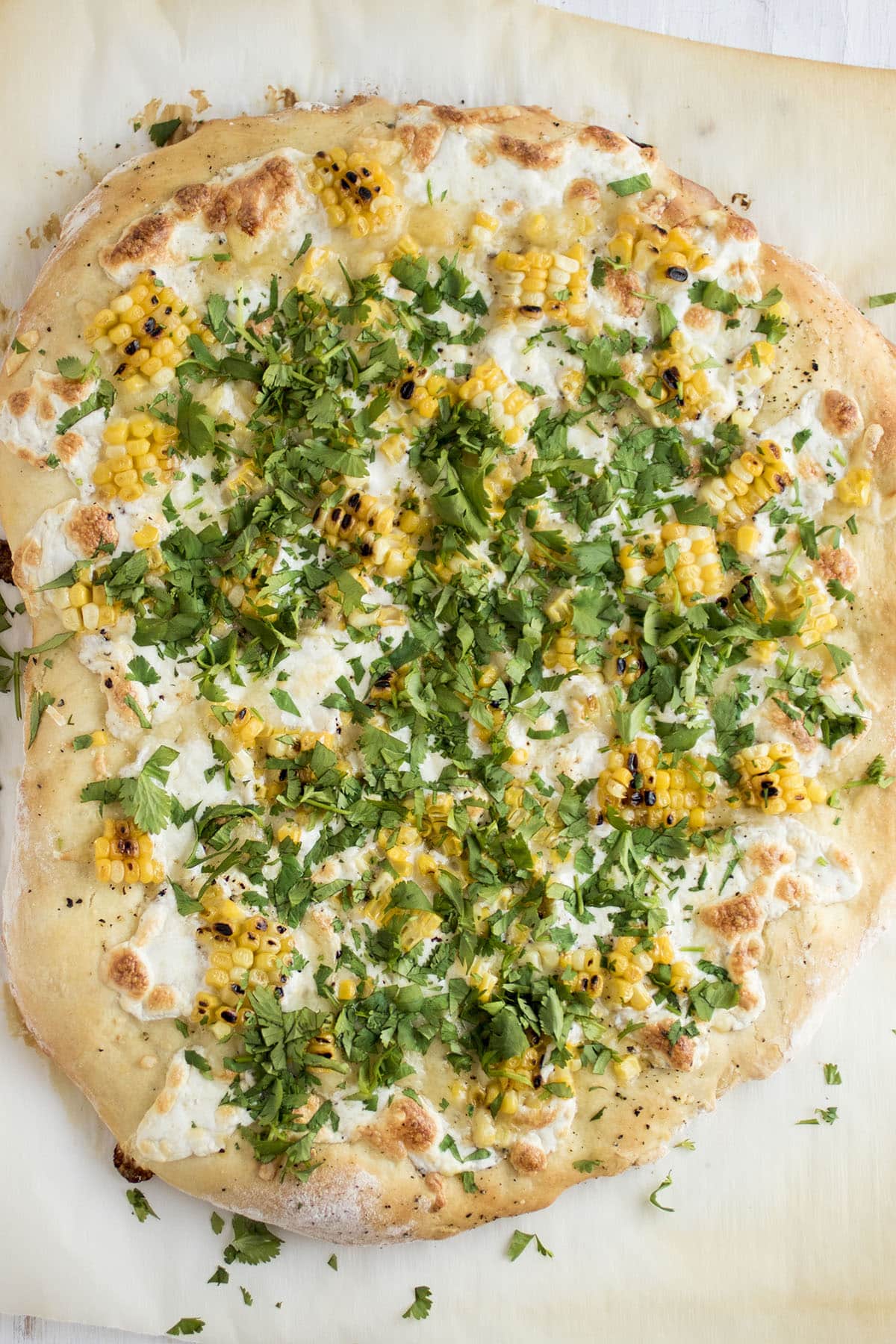 Pizza topped with fresh cilantro on a piece of white parchment paper.