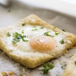 A baked egg on a square of puff pastry, topped with fresh parsley.