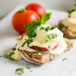 Eggs benedict topped with fresh basil on a white background.