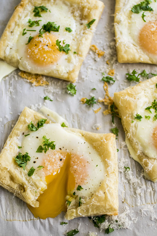 Four puff pastry squares with baked eggs on a baking sheet lined with white parchment paper.