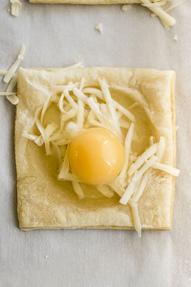 Raw egg on top of puff pastry with shredded white cheese.