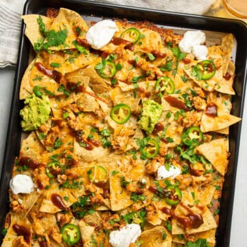 BBQ chicken nachos on a sheet pan with toppings.