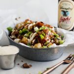 Tater tots in a metal tin topped with cheese, bacon, and green onions.