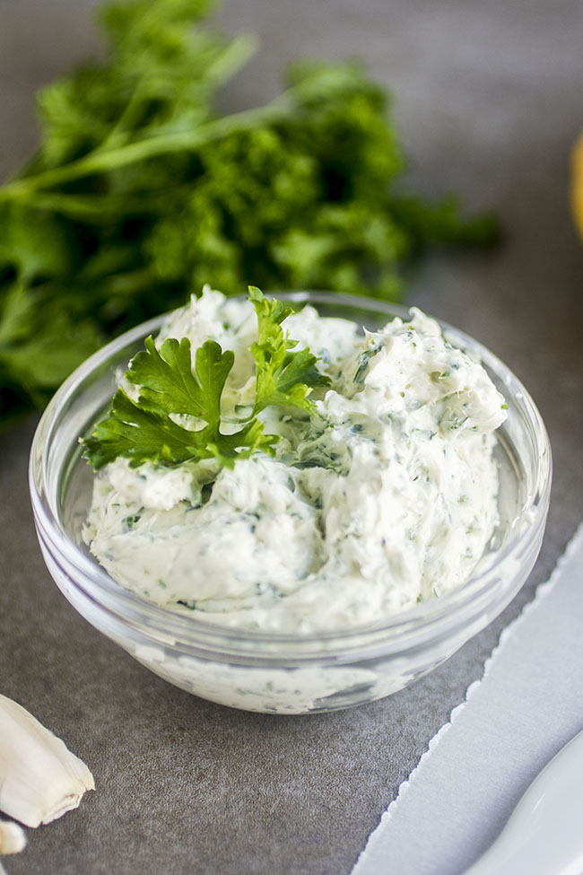 Parsley cream cheese in a small glass bowl, topped with a sprig of fresh parsley.