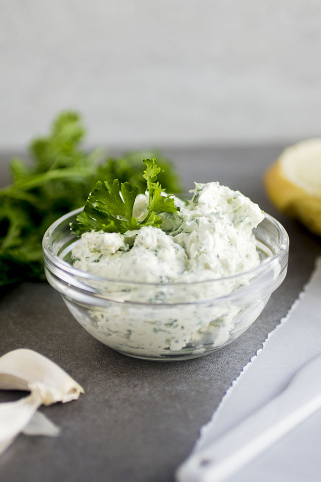 Cream cheese in a small glass bowl next to lemon slices and a bunch of fresh parsley.