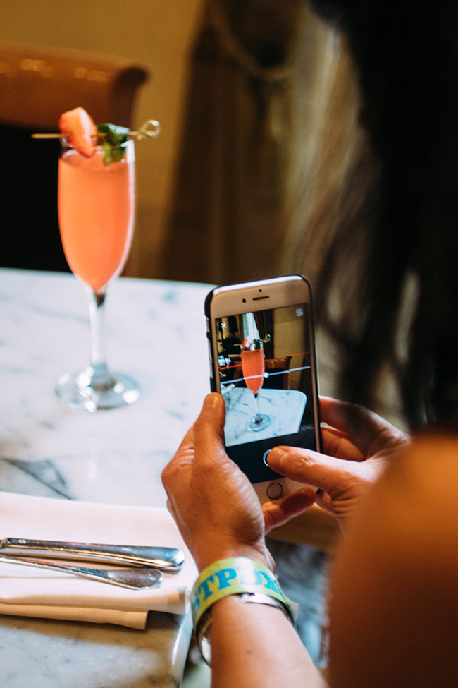 A woman taking a picture of a mimosa with her cell phone.