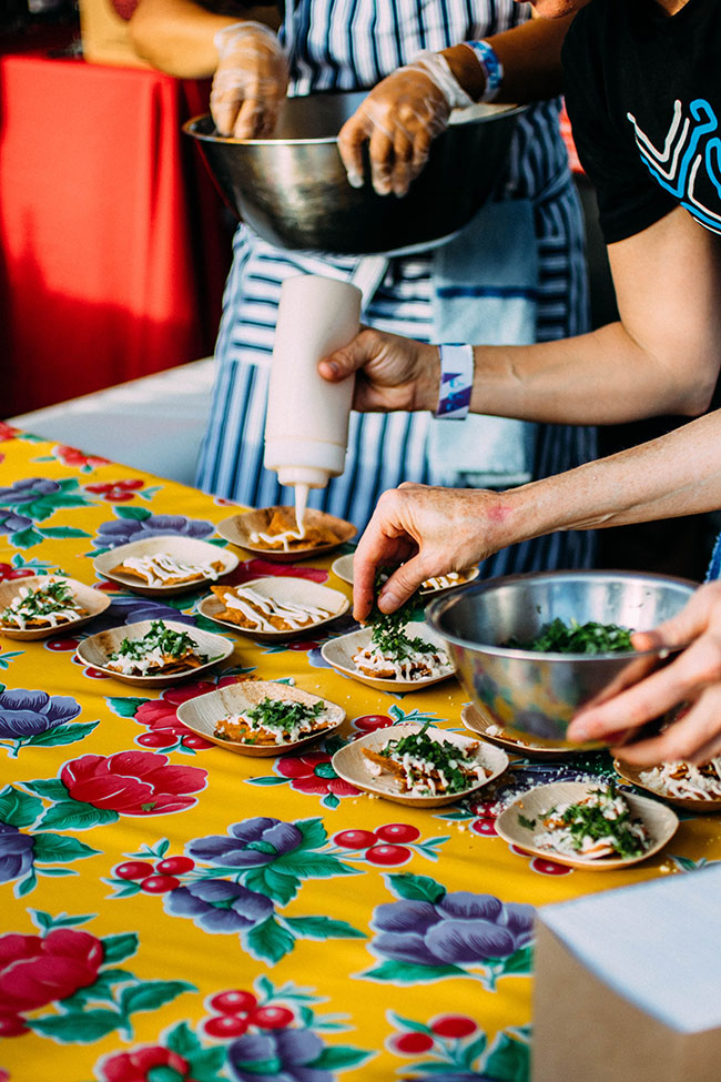 Chefs drizzling crema over small plates of nachos.