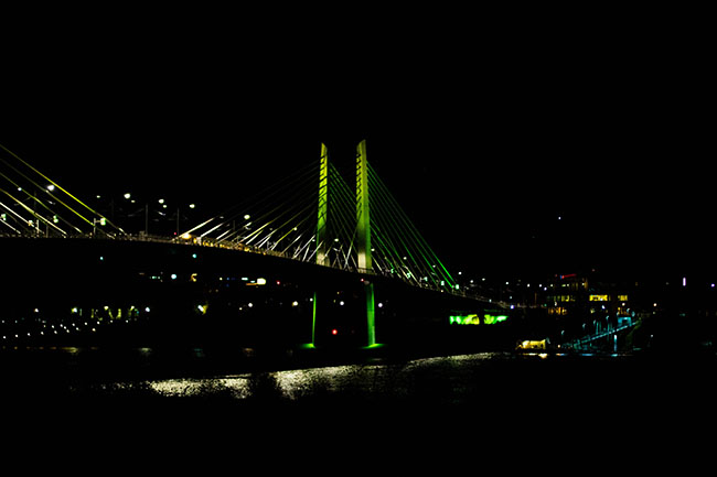 Tillikum bridge in Portland lit up in green lights at nighttime.