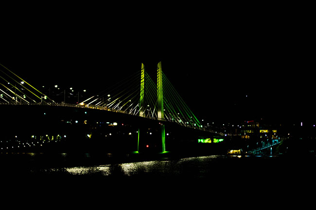 Tillikum bridge in Portland lit up in green lights at nighttime.