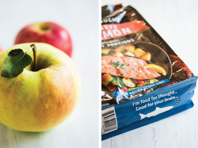 Two apples on a white background next to a bag of frozen sockeye salmon fillets.