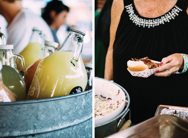 A woman holds a small pulled pork sandwich next to a metal tin filled with bottles of lemonade.