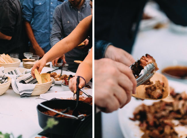 Attendees use tongs to fill their plates with barbecue from a buffet table.