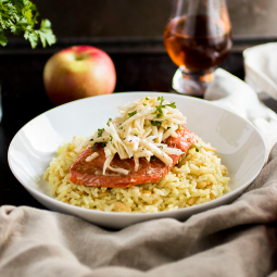 Rice pilaf topped with a salmon fillet and coleslaw in a shallow white bowl.