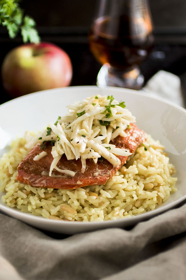 Shallow white bowl filled with rice pilaf, topped with a baked piece of salmon and sliced apples.