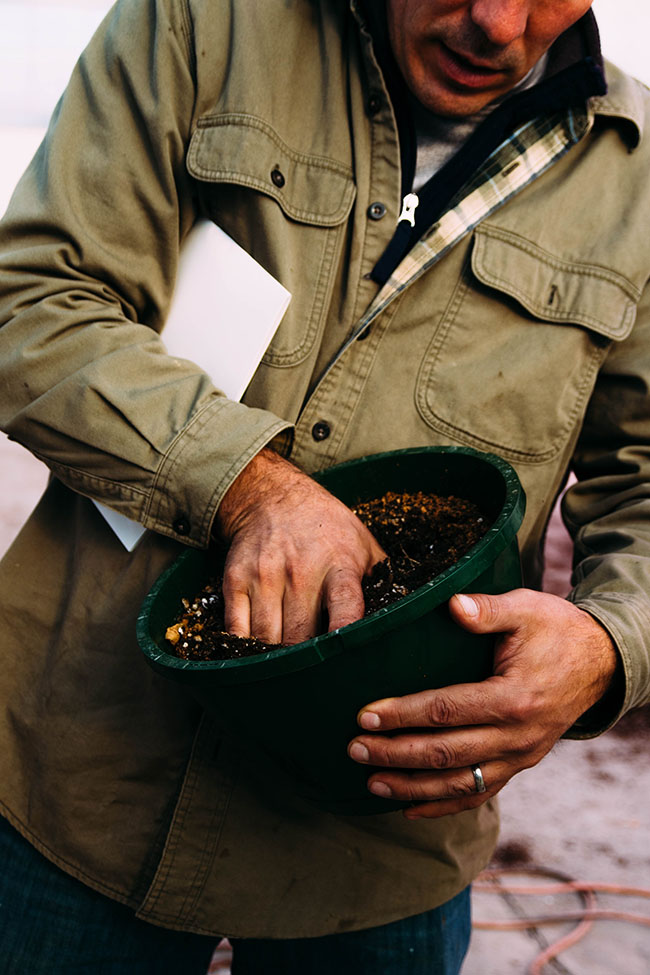 A farmer reaches into a pot filled with dirt.