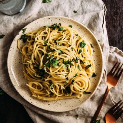 Spaghetti with herbs on a light brown plate next to a tan napkin.