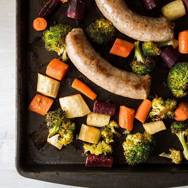 Cooked sausage and roasted veggies on a dark sheet pan.