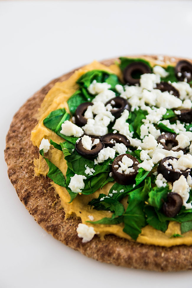 Hummus, spinach, black olives and feta cheese on a piece of wheat pita bread.