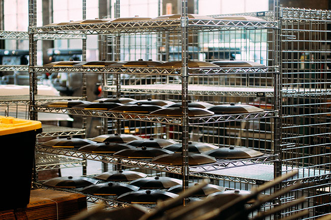 Rows of wire shelves at the Finex factory, each holding cast iron skillets and lids.