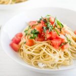 Pasta topped with tomatoes and basil in a shallow white bowl.