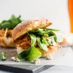 Shredded chicken sandwich with fresh arugula and blue cheese on a white background.