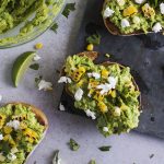 Avocado toast with goat cheese and grilled corn on a light grey table.