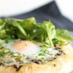 Close up of pizza topped with fresh arugula and a baked egg.