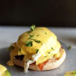 Poached egg on an english muffin, topped with hollandaise sauce and fresh herbs.