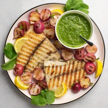 Grilled barramundi on a white plate with radishes and pesto.
