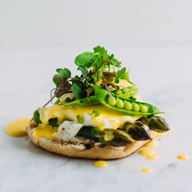 Eggs benedict on a white surface, topped with microgreens.