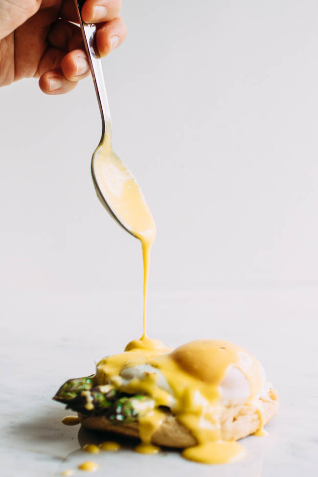 Spoon drizzling hollandaise over eggs benedict.