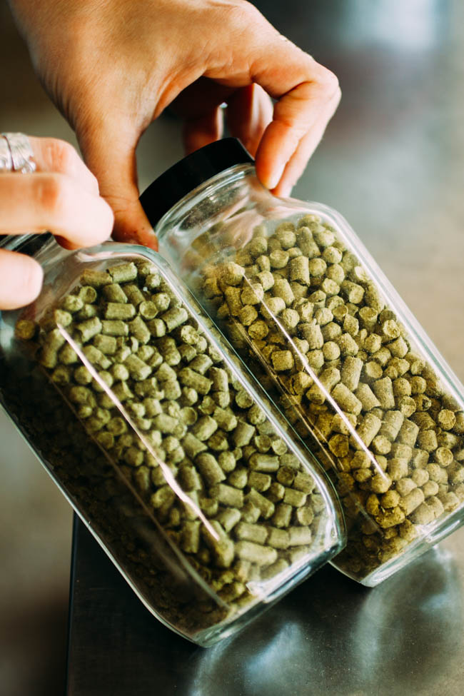 Two glass bottles filled with various dried hop pellets.