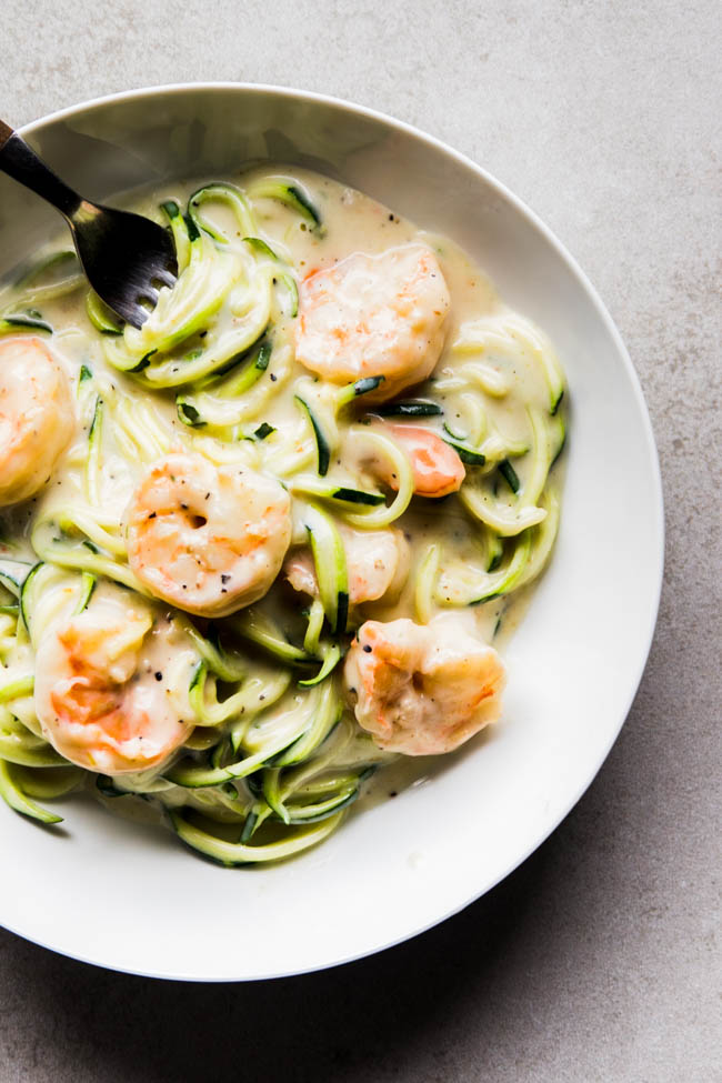 Zoodle shrimp alfredo in a shallow white bowl on a grey table.