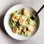 Spiralized zucchini noodles and cooked shrimp in a white bowl.