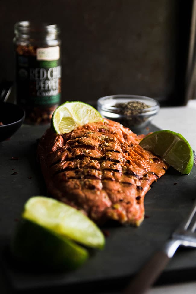Grilled salmon fillet on a slate serving platter with lime wedges.