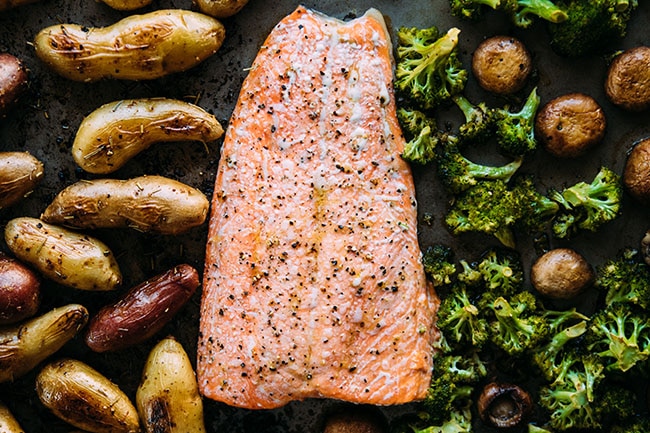 Baked salmon fillet on a sheet pan with roasted fingerling potatoes, broccoli, and mushrooms.