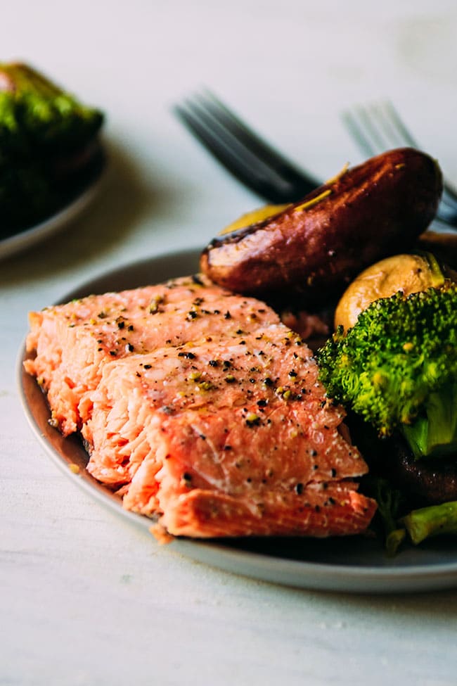 A slice of roasted salmon on a plate with roasted potatoes and broccoli.