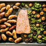 Overhead view of baked salmon, fingerling potatoes, and roasted broccoli on a sheet pan.