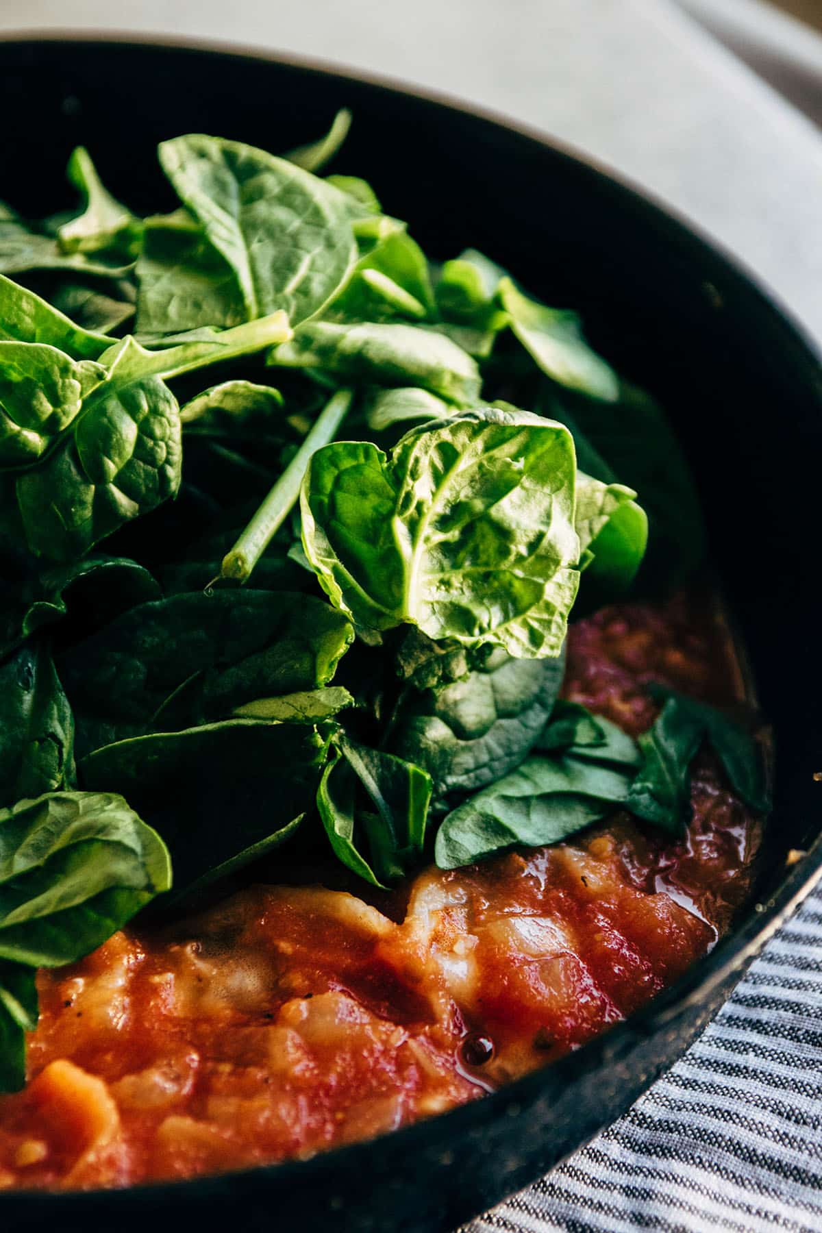 Adding fresh spinach to a skillet with shrimp and tomato sauce.
