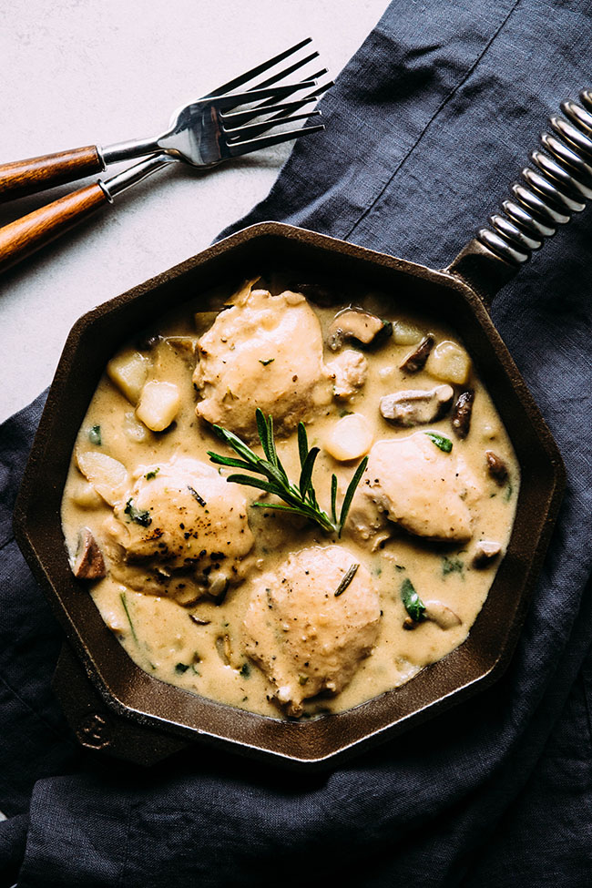 Overhead view of a cast iron skillet filled with creamy chicken and potatoes, next to a blue napkin.