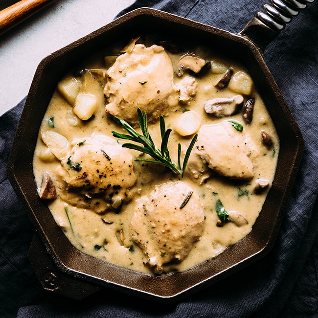 Aerial view of chicken and potatoes in a cast iron skillet, topped with a sprig of fresh rosemary.