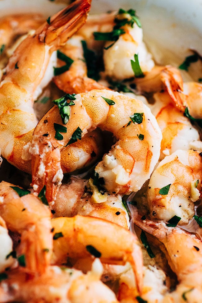 Baked shrimp topped with chopped parsley in a white baking dish.