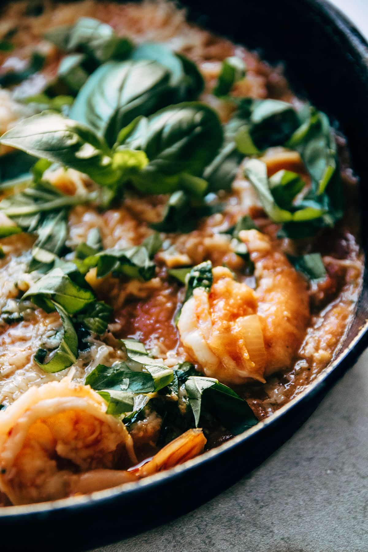 Close up of cooked shrimp in a skillet with tomato sauce and spinach.