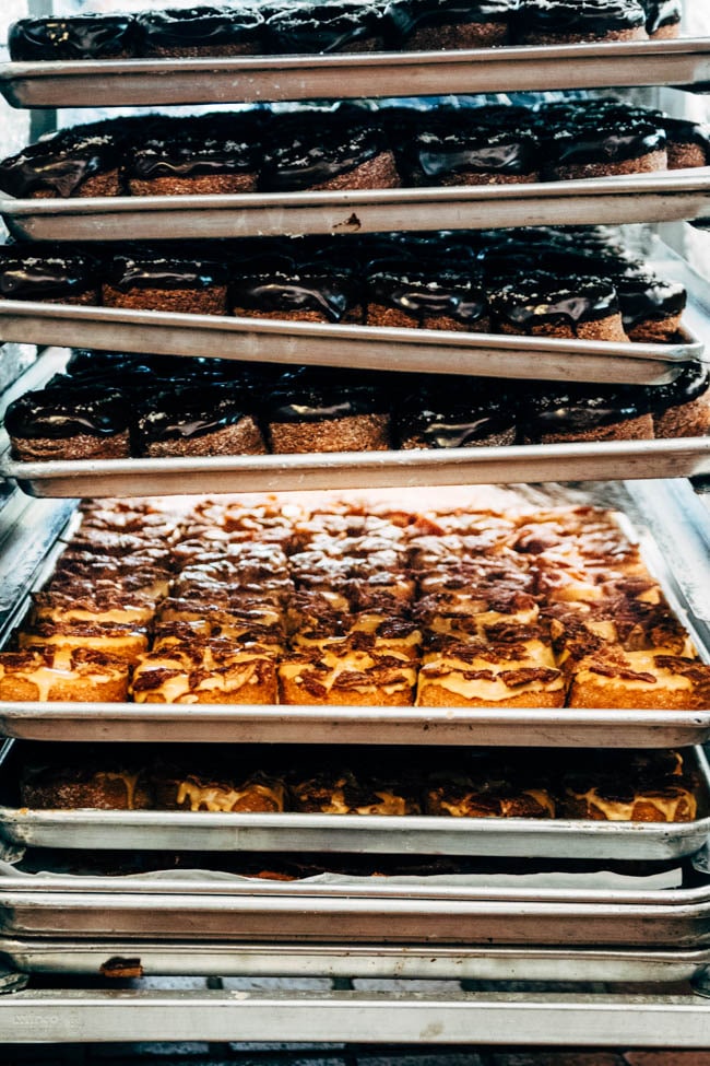 Five trays of fresh donuts stacked on a sheet pan rack.