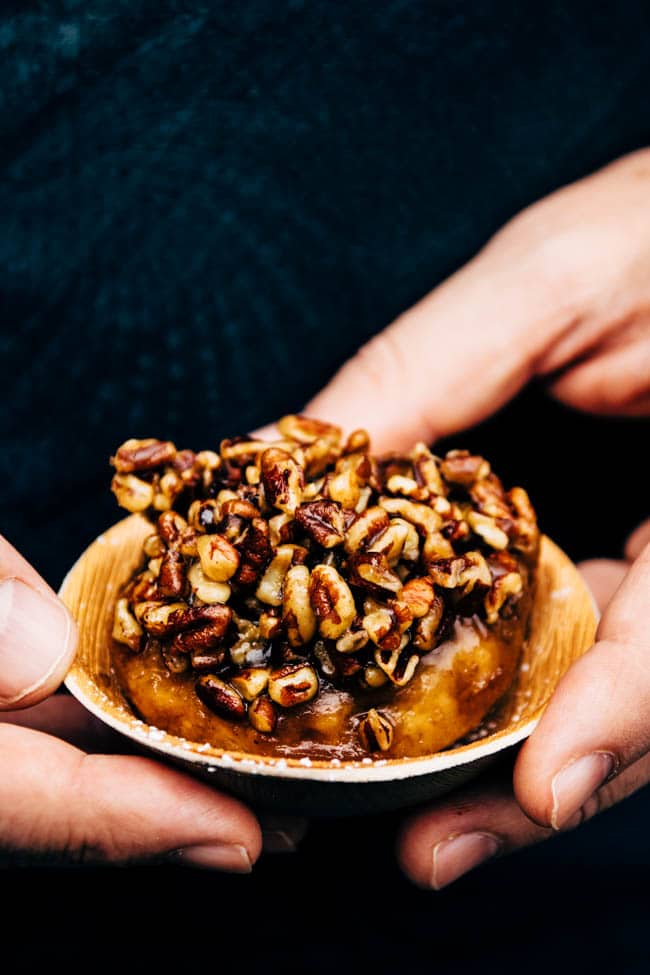 Hands holding a cinnamon bun on a small wooden plate.