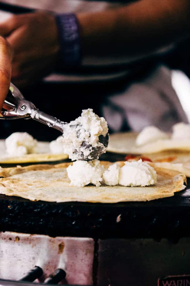 Metal scoop placing scoops of ricotta on a small crepe.