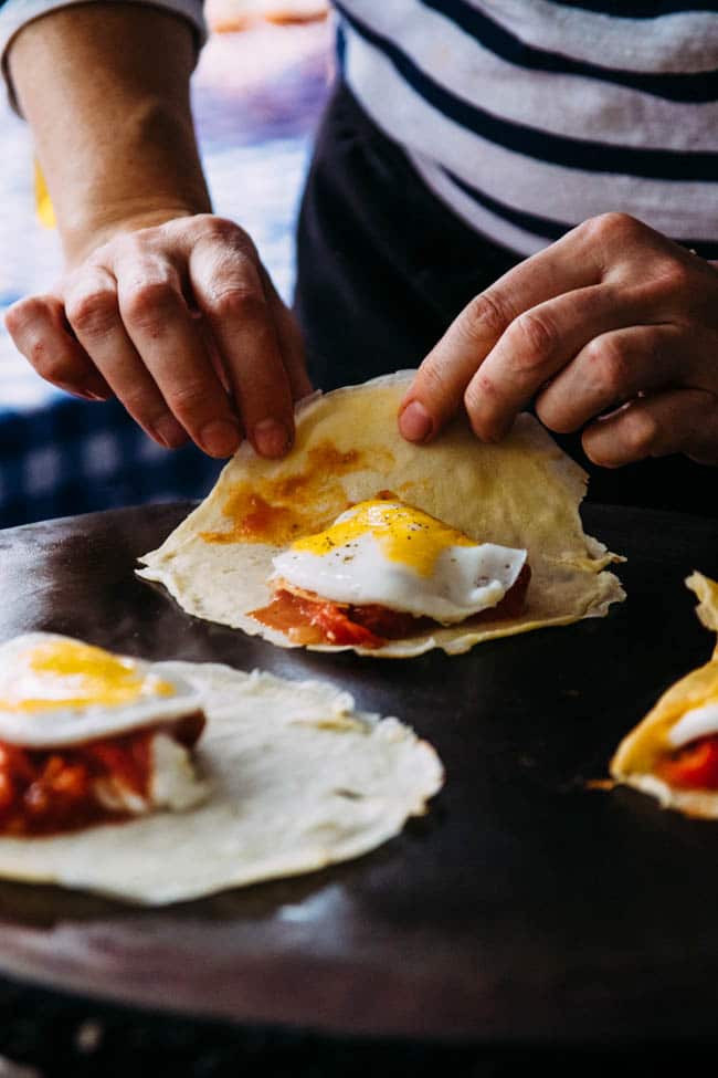 Hands folding a breakfast crepe with a fried egg inside.