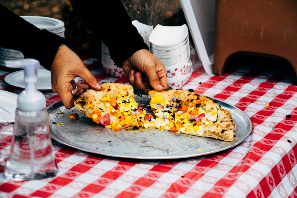 Hands lifting pieces of pizza off of a metal pizza dish.